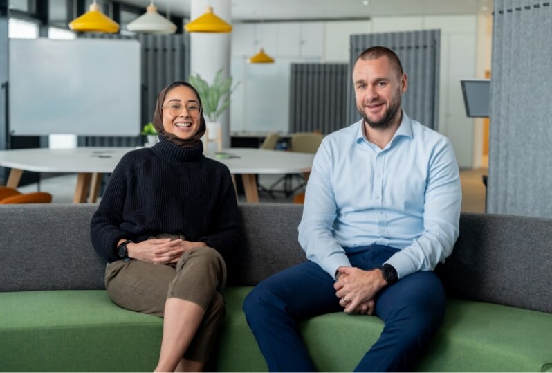 Two people smiling on sofa in office