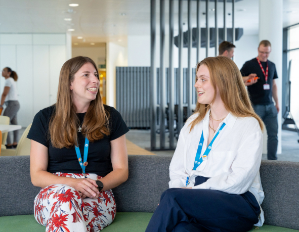 Two colleagues smile while having a conversation on the couch